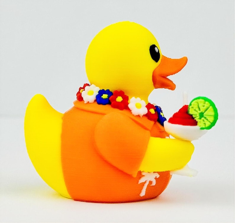 May include: A yellow rubber duck wearing an orange shirt with a white palm tree print and a colorful floral lei around its neck. The duck holds a white cocktail glass containing a red drink garnished with a bright green lime slice.