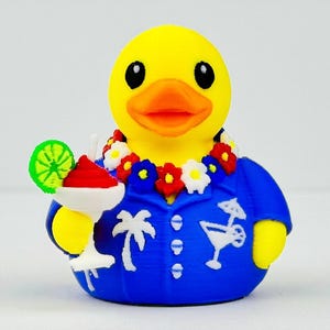 May include: A yellow rubber duck wearing a blue button-down shirt with white palm tree and cocktail glass patterns. The duck has a floral lei around its neck and is holding a white cocktail glass with a red drink and a green lime slice garnish.