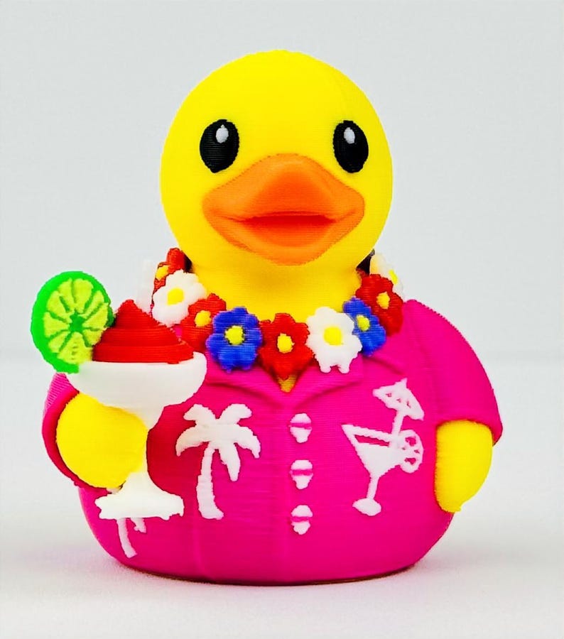 May include: A yellow rubber duck wearing a bright pink shirt with white palm tree and cocktail graphics. The duck has an orange beak, black eyes, a colorful floral lei around its neck, and holds a white cocktail glass with a red drink and lime.