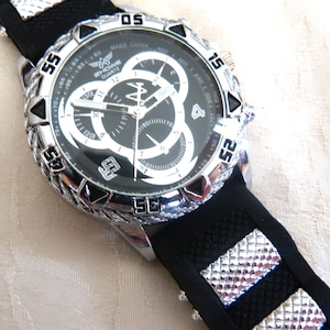 May include: A black and silver wristwatch with a black dial and silver accents. The watch has a black rubber strap with silver embellishments. The watch face displays the text "HOWE QUARTZ" and "MADE CHINA".