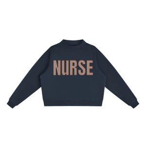 Puede incluir: Una sudadera de manga larga en color azul marino oscuro con cuello alto y puños acanalados. La palabra NURSE está impresa en el pecho en un tono beige claro, con un patrón repetitivo de pequeños puntos blancos que rellenan las letras.
