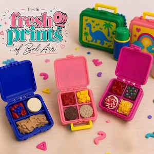 May include: Three miniature plastic lunch boxes in blue and pink, each containing small food-shaped erasers. The text "THE fresh prints of Bel-Air" is visible. The lunch boxes feature compartments filled with tiny replicas of cookies, fruit, and snacks.