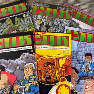 May include: A collection of comic books featuring the title "H!" in large green and red letters. The comics depict various science fiction scenes, including spaceships and futuristic characters. The text "Flagship of the Interstellar Rescue Foundation" is also visible.