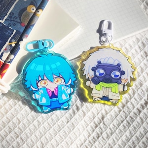 May include: Two acrylic keychains featuring chibi-style anime characters. The left keychain has a blue-haired character in a blue jacket with a light blue clasp. The right keychain features a white-haired character wearing a dark gas mask and a green scarf with a white clasp.