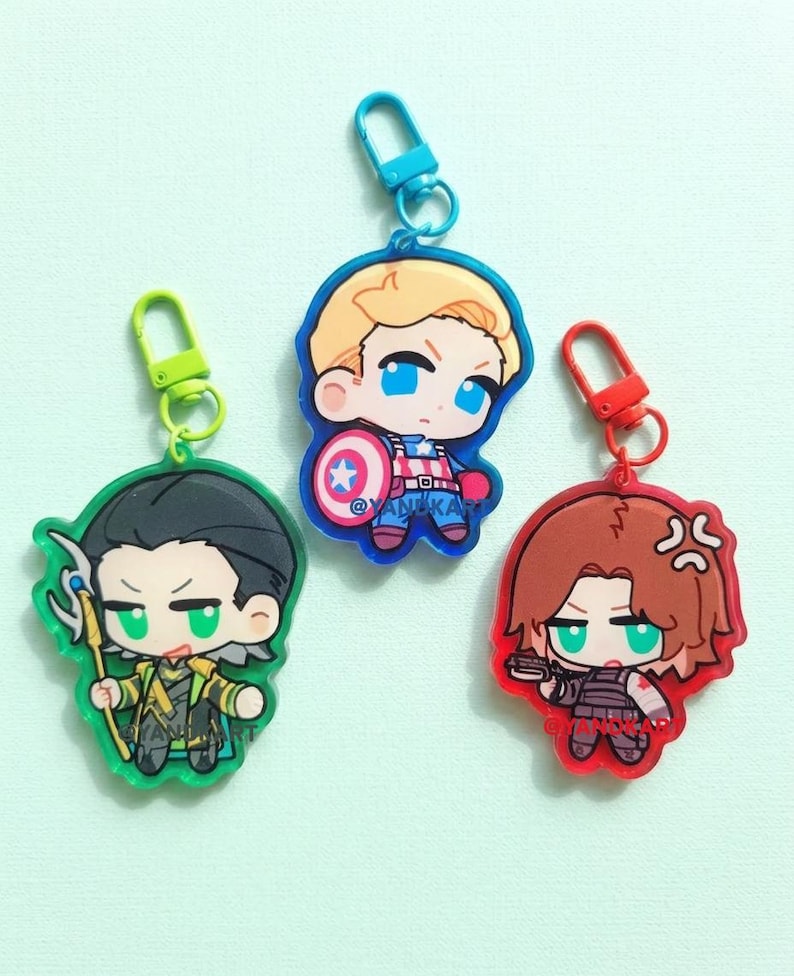 May include: Three acrylic keychains featuring chibi-style characters with colored plastic clasps. One keychain depicts a character with black hair and a green staff, one with blonde hair and a shield, and one with brown hair holding a small black weapon.