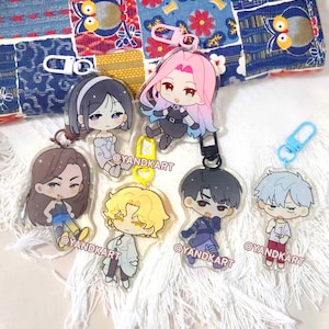 May include: Six acrylic keychains featuring chibi-style anime characters with colorful hair and outfits, each attached to a plastic clasp. The characters have distinct designs and the text @YANDKART is printed on each clear acrylic charm.