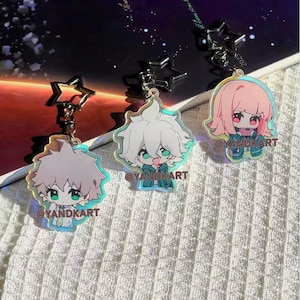 May include: Three iridescent acrylic keychains featuring anime-style characters with star-shaped silver metal clasps. Each charm displays a unique character illustration with the text @YANDKART printed in brown on the front surface of the acrylic.