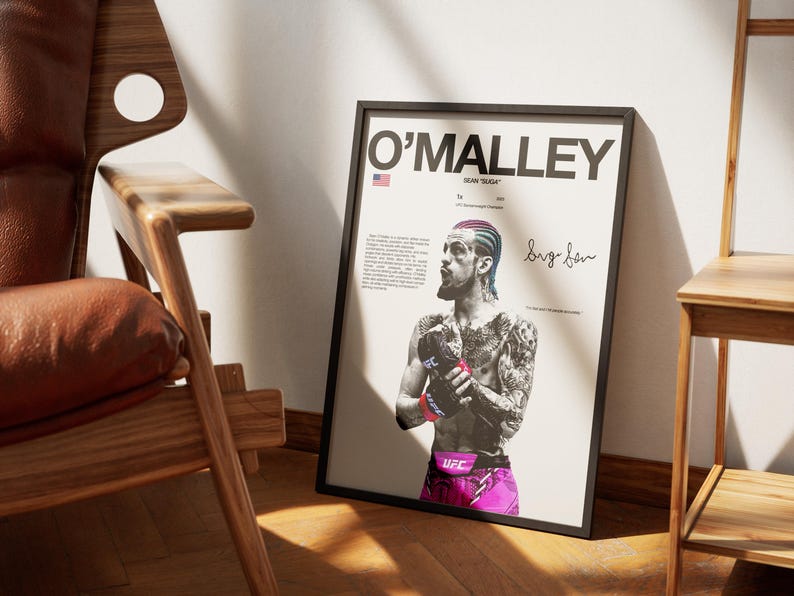 Op de afbeelding: Een ingelijste poster met een zwart-wit portret van UFC-vechter Sean O'Malley met gekleurd haar, handschoenen en een korte broek. De tekst bevat O'MALLEY, SEAN SUGA en een handtekening. Het ontwerp bevat een klein icoon van de Amerikaanse vlag.