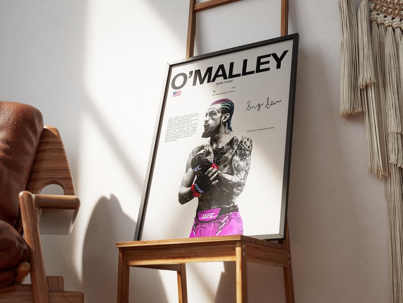 Op de afbeelding: Een ingelijste poster met een zwart-wit portret van Sean O'Malley met gekleurd haar, dragend UFC-handschoenen en een roze broek. De tekst luidt O'MALLEY, SEAN "SUGA" en bevat een handtekening, een kleine Amerikaanse vlag en beschrijvende tekst.