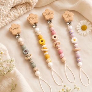 May include: Four pacifier clips featuring wooden flower-shaped clips engraved with the names Emma, Olivia, Sophia, and Isla. Each clip is attached to a string of silicone and wooden beads in various colors, including sage green, yellow, pink, and lavender, with floral-shaped bead accents.
