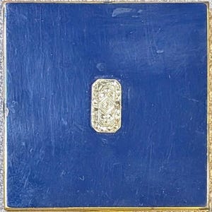 May include: A square compact case with a deep blue enamel finish and a gold-toned metal border. Centered on the lid is an elongated octagonal gold-toned metal inlay featuring a geometric pattern with small clear stones set within the design.