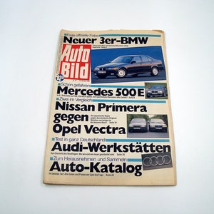 May include: A vintage magazine titled "Auto Bild" with a dark blue BMW on the cover. The magazine features articles on Mercedes, Nissan, Opel, and Audi. The cover is aged with visible wear and tear.