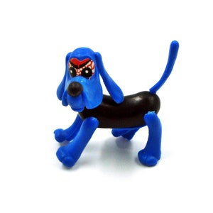 Könnte beinhalten: Ein blau-brauner Spielzeughund mit Cartoon-Design. Der Hund hat blaue Ohren, Beine und einen Schwanz sowie einen braunen Körper. Das Gesicht hat ein rot-weißes Design um die Augen.