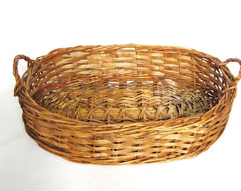 Könnte beinhalten: Ovaler Weidenkorb mit zwei Griffen. Der Korb besteht aus hellbraunem, gewebtem Material und hat eine strukturierte Oberfläche. Die Griffe sind eng gewebt und gebogen. Der Korb ist leer und steht auf weißem Hintergrund.