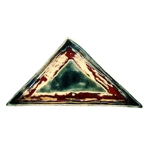 May include: A triangular ceramic dish with a layered design. The dish has a dark teal centre, surrounded by a cream-coloured layer, and a deep red outer edge. The edges are outlined in a dark blue.
