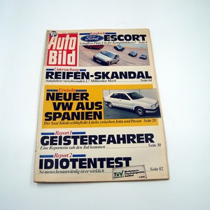 May include: A vintage German magazine titled "Auto Bild" with articles on cars. The cover features headlines in German, including "REIFEN-SKANDAL" and "NEUER VW AUS SPANIEN." The magazine has images of cars and text.