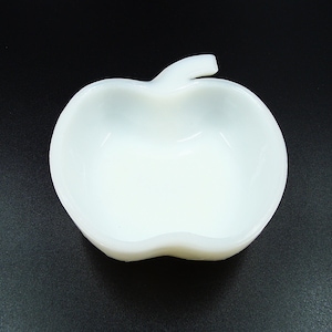 Puede incluir: Un plato blanco en forma de manzana con un tallo. El plato está hecho de un material liso y opaco y tiene un cuenco poco profundo. El plato probablemente se utiliza para servir pequeñas porciones de comida o como objeto decorativo.