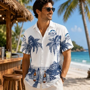 May include: A white short-sleeved button-down shirt featuring a blue ink-style print of palm trees, a surfboard, and Busch Light beer cans. The shirt displays the Busch Light logo on the chest and sleeves, with a classic collar and front buttons.