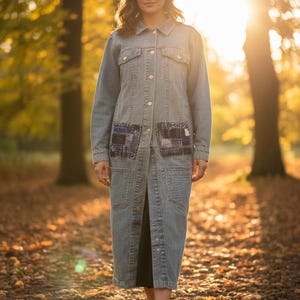 May include: A long, light-wash denim coat featuring a classic collar, button-down front, and long sleeves. The garment includes two chest pockets and two lower pockets, with dark blue patterned patchwork fabric accents on the chest pockets.
