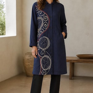 May include: A navy blue long-sleeve coat featuring a button-down front, a collar, and side pockets. The right side of the coat is decorated with an intricate, curved embroidery pattern in cream and red thread, showcasing circular and swirling motifs.