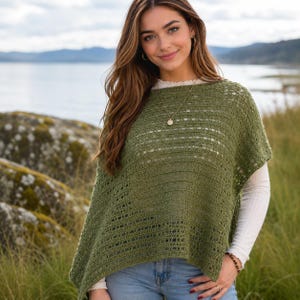 Op de afbeelding: Een olijfgroene gehaakte poncho met een gestructureerd opengewerkt patroon en horizontale strepen. Het kledingstuk heeft een brede boothals en korte, losse mouwen, gedragen over een wit shirt met lange mouwen en een lichtblauwe spijkerbroek.