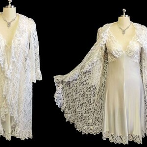 K&ouml;nnte beinhalten: Eine wei&szlig;e Spitzenrobe mit langem, flie&szlig;endem Design. Die Robe hat einen tiefen V-Ausschnitt und lange &Auml;rmel. Die Robe wird mit einem passenden Unterkleid gezeigt.