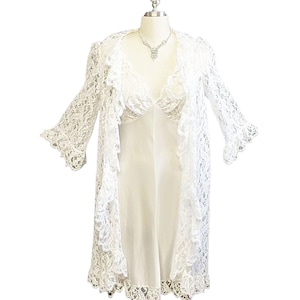 K&ouml;nnte beinhalten: Wei&szlig;es Kleid mit Spitzen&uuml;berwurf und Satinunterkleid. Das Kleid hat einen V-Ausschnitt und lange &Auml;rmel.