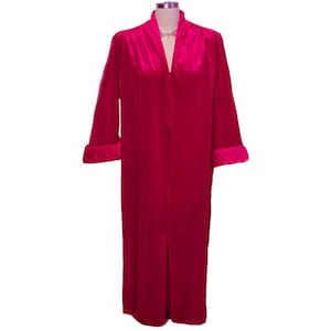 May include: A long, pink velvet robe with a shawl collar and long sleeves. The robe has a single button closure at the front and a slit up the back.