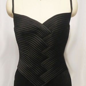 May include: A black satin evening gown with a pleated bodice and a sweetheart neckline. The gown has thin spaghetti straps and a fitted silhouette.