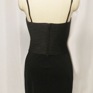 May include: A black sleeveless dress with a fitted bodice and a flowing skirt. The bodice has a pleated design and a zipper closure in the back.