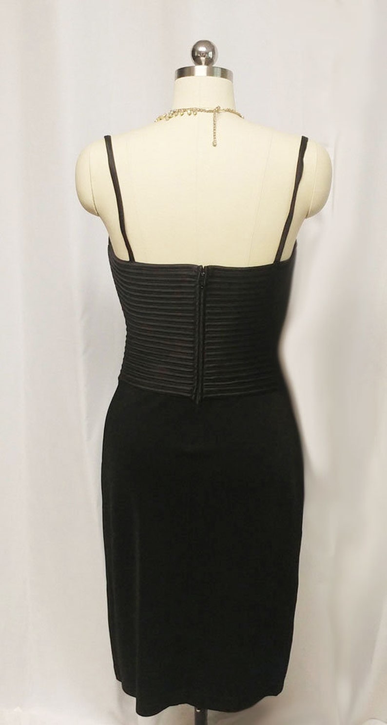 May include: A black sleeveless dress with a fitted bodice and a flowing skirt. The bodice has a pleated design and a zipper closure in the back.