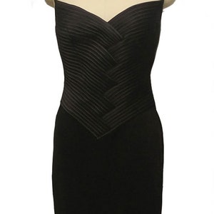 May include: A black sleeveless dress with a pleated bodice and a fitted skirt. The dress is on a mannequin and has a rhinestone necklace.