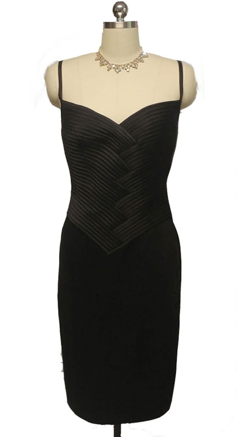May include: A black sleeveless dress with a pleated bodice and a fitted skirt. The dress is on a mannequin and has a rhinestone necklace.