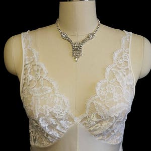 K&ouml;nnte beinhalten: Ein wei&szlig;es Spitzen-Schlafkleid mit einem zarten V-Ausschnitt und einer Strasskette.