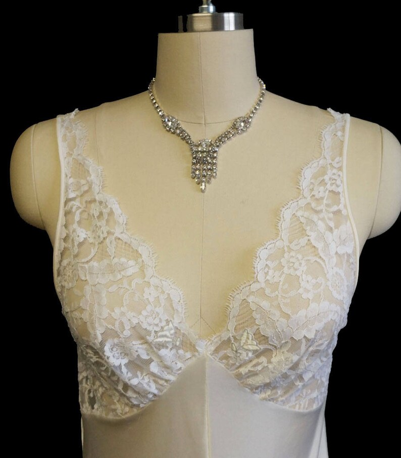 K&ouml;nnte beinhalten: Ein wei&szlig;es Spitzen-Schlafkleid mit einem zarten V-Ausschnitt und einer Strasskette.