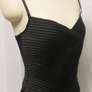 May include: A black, sleeveless dress with a pleated bodice and a fitted skirt. The dress has a simple, elegant design.