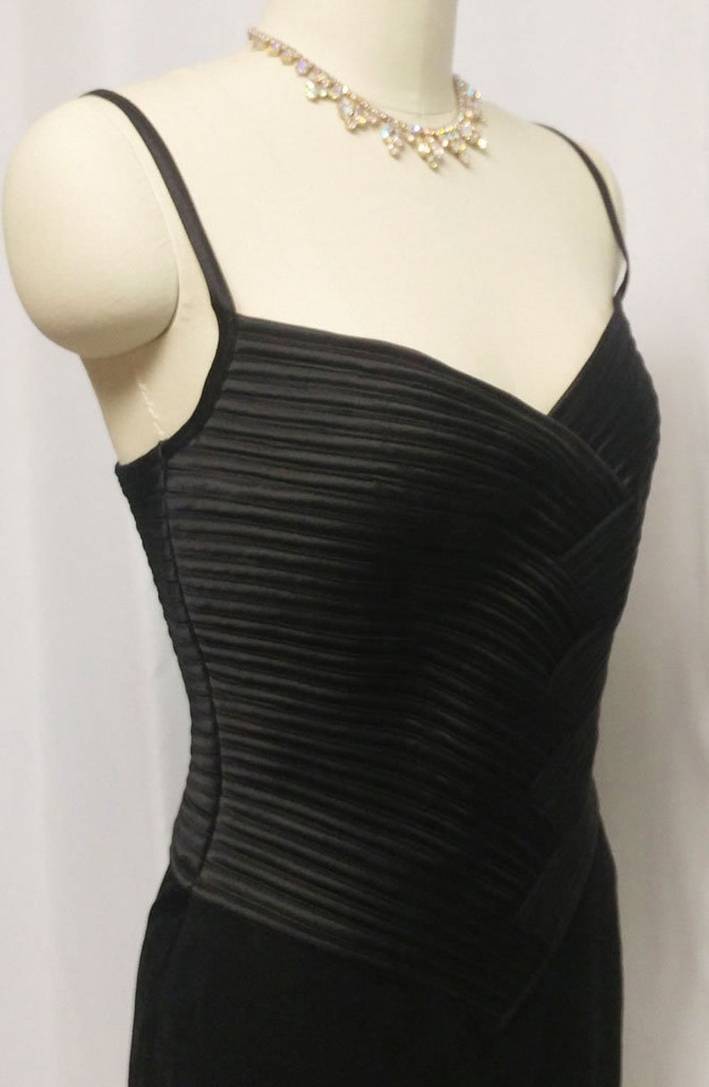 May include: A black, sleeveless dress with a pleated bodice and a fitted skirt. The dress has a simple, elegant design.