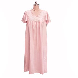 May include: A light pink nightgown displayed on a mannequin. The floor-length gown features short, ruffled sleeves and a V-neckline with white lace detailing. A delicate pearl necklace adorns the mannequin's neck. The fabric appears soft and flowing.