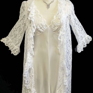 K&ouml;nnte beinhalten: Wei&szlig;e Spitzenrobe mit passendem Unterkleid. Die Robe hat lange &Auml;rmel und einen R&uuml;schenkragen. Das Unterkleid hat einen V-Ausschnitt und ist &auml;rmellos.