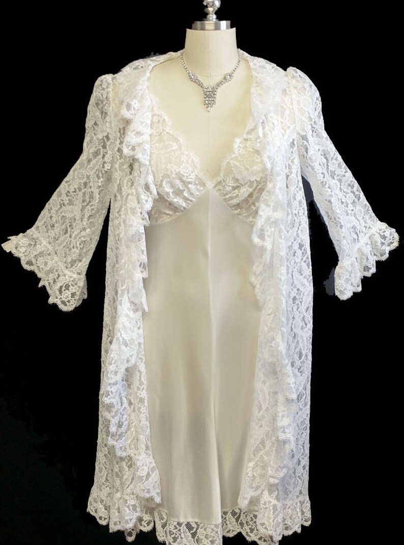 K&ouml;nnte beinhalten: Wei&szlig;e Spitzenrobe mit passendem Unterkleid. Die Robe hat lange &Auml;rmel und einen R&uuml;schenkragen. Das Unterkleid hat einen V-Ausschnitt und ist &auml;rmellos.