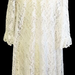 K&ouml;nnte beinhalten: Eine wei&szlig;e Spitzenrobe mit langen &Auml;rmeln und einem R&uuml;schenkragen. Die Robe ist aus zarter Spitze gefertigt und hat eine flie&szlig;ende Silhouette.