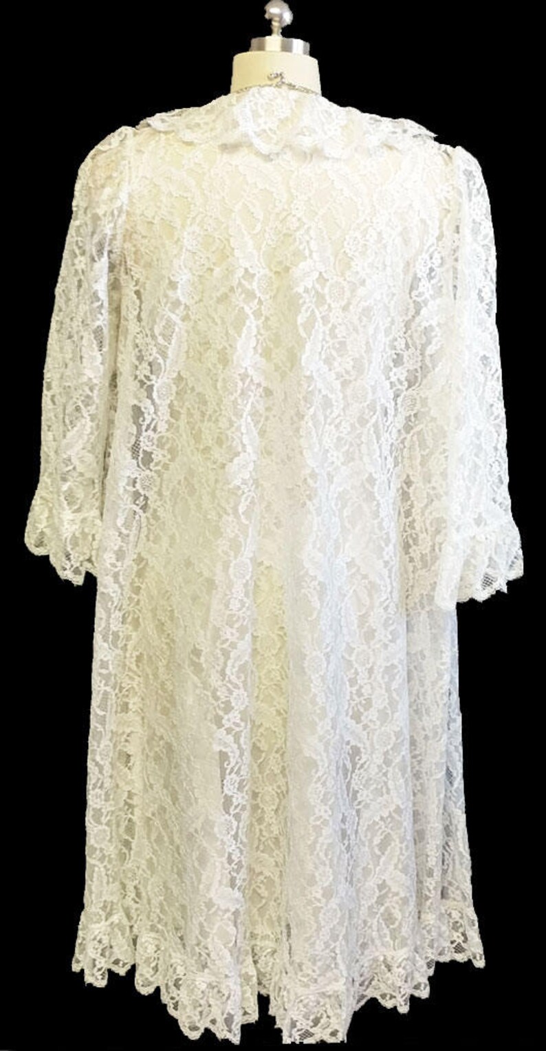K&ouml;nnte beinhalten: Eine wei&szlig;e Spitzenrobe mit langen &Auml;rmeln und einem R&uuml;schenkragen. Die Robe ist aus zarter Spitze gefertigt und hat eine flie&szlig;ende Silhouette.