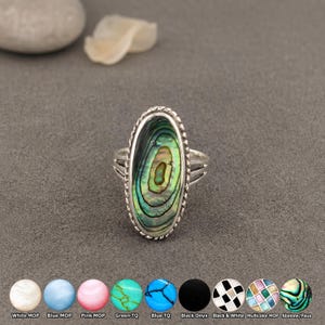 May include: An oval ring featuring an iridescent abalone shell inlay set in a silver-toned metal frame with a twisted rope border. The band has a triple-split design. Below the ring are circular swatches labelled White MOP, Blue MOP, Pink MOP, Green TQ, Blue TQ, Black Onyx, Black & White, Multicolor MOP, and Abalone/Paua.