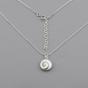 Puede incluir: Un collar de cadena en tono plateado con un colgante circular que presenta una incrustación de concha natural en espiral de color blanco y marrón. El collar incluye una cadena de eslabones finos, un cierre de resorte y una cadena extensora ajustable.