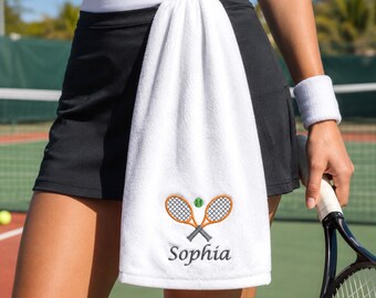 Könnte beinhalten: Ein weißes rechteckiges Handtuch mit einer Stickerei aus zwei gekreuzten orangefarbenen Tennisschlägern und einem grünen Tennisball. Unter den Schlägern ist der Name Sophia in dunkelgrauer Schreibschrift auf den Stoff gestickt.