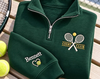 Könnte beinhalten: Ein dunkelgrüner Sweatshirt mit kurzem Reißverschluss und einer Stickerei aus zwei gekreuzten Tennisschlägern, einem Tennisball und dem Schriftzug COURT CLUB. Der Ärmel ist mit dem Namen Bennett über einem Herz und einem Ball bestickt.