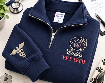 Könnte beinhalten: Ein marineblauer Fleece-Pullover mit Viertelreißverschluss und einem gestickten Logo, das eine Katze, einen Hund, ein Herz und ein Stethoskop zeigt. Der Text lautet Emily VET TECH. Der Ärmel zeigt ein goldenes Caduceus-Symbol mit Pfotenabdruck.