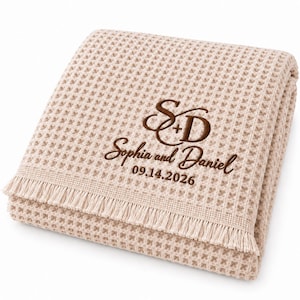 Parchment waffle throw featuring a personalized wedding embroidery positioned near the lower corner.
The design includes a large intertwined “S + D” monogram, “Sophia and Daniel” in script, and the date “09.14.2026” below.
All details are embroidered in deep brown thread for a clear contrast against the light Parchment fabric.
The elegant corner placement creates a personalized monogrammed wedding throw design.