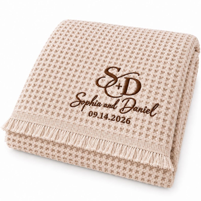 Parchment waffle throw featuring a personalized wedding embroidery positioned near the lower corner.
The design includes a large intertwined “S + D” monogram, “Sophia and Daniel” in script, and the date “09.14.2026” below.
All details are embroidered in deep brown thread for a clear contrast against the light Parchment fabric.
The elegant corner placement creates a personalized monogrammed wedding throw design.