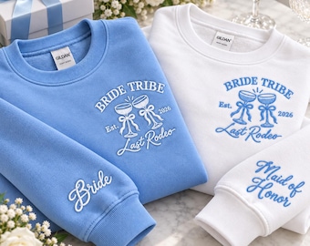 Könnte beinhalten: Ein hellblaues Sweatshirt mit weißer Stickerei Bride Tribe Est. 2026 Last Rodeo und Bride am Ärmel sowie ein weißes Sweatshirt mit blauer Stickerei Bride Tribe Est. 2026 Last Rodeo und Maid of Honor am Ärmel.